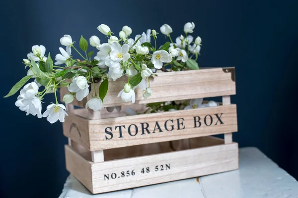 Wooden box for storing things with the inscription Sweet home with an apple flowering branch on a white vintage stool against a dark blue wall. Copy space