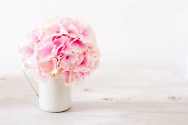 Masanın beyaz dokusuna yerleştirilmiş bir kupada pembe ortanca. Metin için yer.