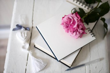 Defterlerde pembe gül çiçeği ve tahta bir taburede alçı kalp. Boşluğu kopyala