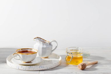 Beyaz fincanda siyah çay, bal kavanozu ve bal kaşığı, beyaz arka planda limon kaplaması.