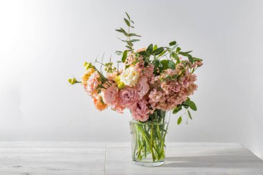 Bir buket pembe ve turuncu lisianthus, antirrhinum ve mutfak masasındaki cam vazoda çeşitli okaliptüs çeşitleri. Metin için boşluk