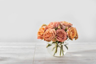 Mutfak masasındaki yuvarlak cam vazoda pembe ve turuncu bir gül buketi. Metin için boşluk