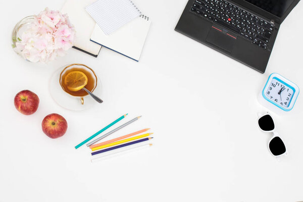 Laptop, notebook, felt-tip pens, watches, sunglasses, a cup of tea with lemon, pencils and a bouquet of hydrangea on the office desk. Frame. Copy space