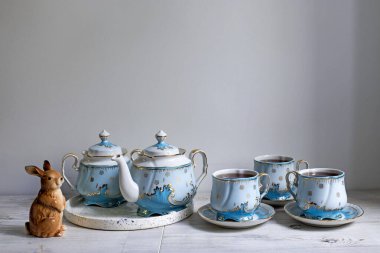 Masanın üzerinde mavi bir porselen çay seti. Çaydanlık ve bir fincan çay. Tavşan heykeli.