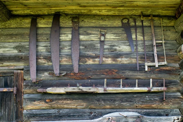 古い木の家の壁には古いのこぎりや作業道具がかかっています — ストック写真