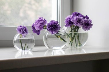 Masa süsü olarak farklı boyutlarda dört yuvarlak cam vazolarda leylak karanfiller.