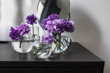 Masa süsü olarak farklı boyutlarda dört yuvarlak cam vazolarda leylak karanfiller.