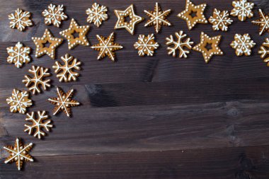 Yüksek açılı yakın plan güzel bir Noel süslemesi manzarası. Tahta bir masada kar taneleri, oklar, yıldızlar ve kalpler şeklinde zencefilli kurabiyeler.