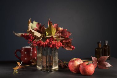 Bir vazo içinde olgun böğürtlen bulunan kırmızı viburnum dalları koyu mavi duvarın karşısındaki masada duruyor. Kırmızı bardak beyaz daireler ve dikenli dutlar..
