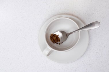 Kavram. Boş beyaz seramik bardak ve bej tahta bir masanın içindeki kaşıkta kurumuş hazır kahve tabağı. Boşluğu kopyala