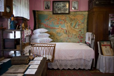 Brateevo, Vologda bölgesi - 20 Temmuz 2020, geleneksel Rus kulübesinin içi. Yastıklı yatak, duvarda aile resimleri, köşede gardırop, heykelciklerle dolu bir raf. Üst oda ve yatak odası.