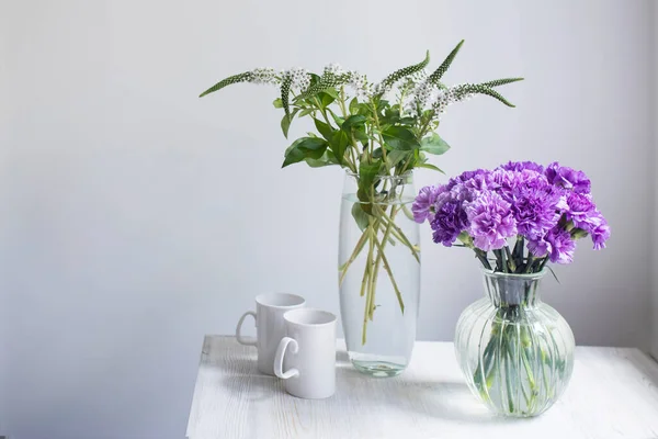 在四个圆形玻璃瓶中的紫丁香康乃馨的新娘花束大小各不相同 就像桌上的装饰品 两杯白茶 — 图库照片