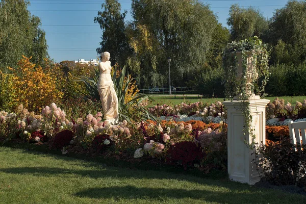 The plaster statue is reflected in a small pond lined with yellow and red chrysanthemums and hydrangeas.