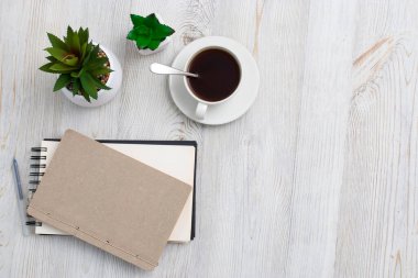 Ofis masası iş yeri, defter, yapay bitki ve fotokopi alanı olan kahve fincanı..