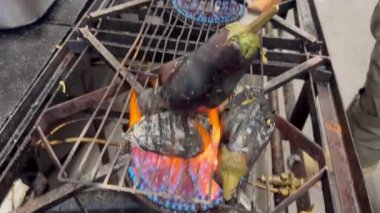 Grilling eggplants over an open flame. A hand with a fork flips the eggplants.