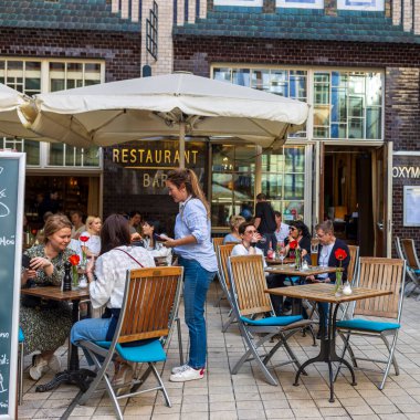 Berlin, Almanya, 5 Mayıs 2025, Hackesche Hfe 'nin avlusundaki işlek sokak restoranı. İnsanlar büyük şemsiyeler altında açık masalarda yemek yiyor, şehir avlusunun atmosferinin tadını çıkarıyorlar. Bir sunucu sipariş alıyor