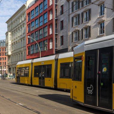 Berlin, Almanya, 5 Mayıs 2025, caddelerde sarı tramvaylı şehir hayatı, modern ve geleneksel Avrupa binalarının yanından geçiyor. Ön planda bir kişi bisiklet sürüyor ve kaldırımda diğer yayalar görülebilir.. 