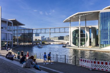 Berlin, Almanya, 5 Mayıs 2025, Berlin 'den Marie-Elisabeth-Lueders-Haus ve Paul-Loewe-Haus, Spree Nehri üzerindeki yaya köprüsü ile bağlandılar. İnsanlar nehir kıyısında turist botu geçerken dinleniyor. 