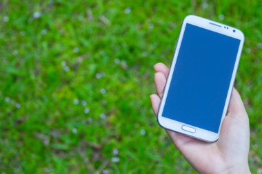 Akıllı bir telefon kullanarak kadın elinin yakın plan çekimi, yeşil doğa geçmişi