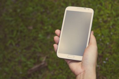 Akıllı bir telefon kullanarak kadın elinin yakın plan çekimi, yeşil doğa geçmişi