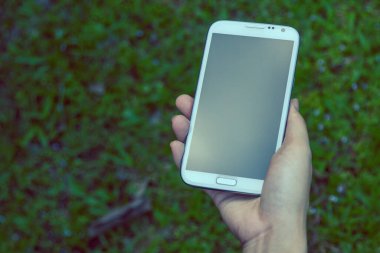 Akıllı bir telefon kullanarak kadın elinin yakın plan çekimi, yeşil doğa geçmişi