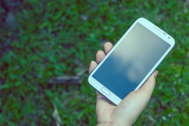 Akıllı bir telefon kullanarak kadın elinin yakın plan çekimi, yeşil doğa geçmişi