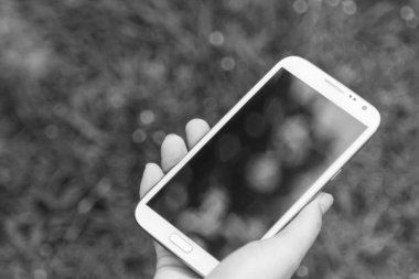 Akıllı bir telefon kullanarak kadın elinin yakın plan çekimi, yeşil doğa geçmişi