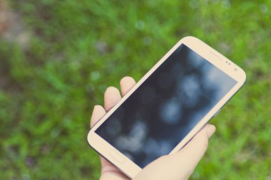 Akıllı bir telefon kullanarak kadın elinin yakın plan çekimi, yeşil doğa geçmişi