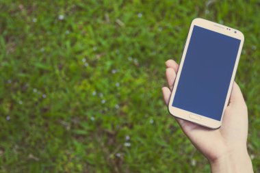 Akıllı bir telefon kullanarak kadın elinin yakın plan çekimi, yeşil doğa geçmişi