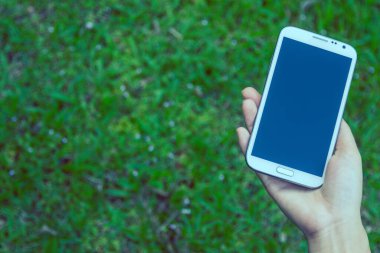 Akıllı bir telefon kullanarak kadın elinin yakın plan çekimi, yeşil doğa geçmişi