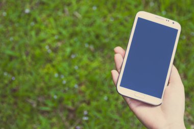 Akıllı bir telefon kullanarak kadın elinin yakın plan çekimi, yeşil doğa geçmişi