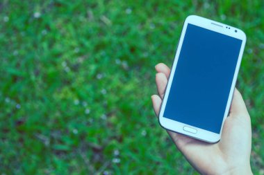 Akıllı bir telefon kullanarak kadın elinin yakın plan çekimi, yeşil doğa geçmişi