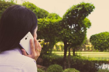 Akıllı bir telefon kullanarak kadın elinin yakın plan çekimi, yeşil doğa geçmişi