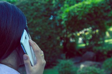 Akıllı bir telefon kullanarak kadın elinin yakın plan çekimi, yeşil doğa geçmişi