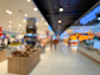 Bir alışveriş merkezi koridorunun bulanık görüntüsü, modern bir perakende ortamın canlı atmosferini gözler önüne seriyor. İnsanlar çeşitli mağazalara girip çıkarken görülüyorlar.