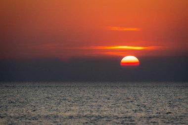 Sakin bir günbatımı sahnesi ufkun altında yavaşça kayboluyor, sakin okyanusun üzerine yumuşak, pembe ve turuncu renkler döküyor..