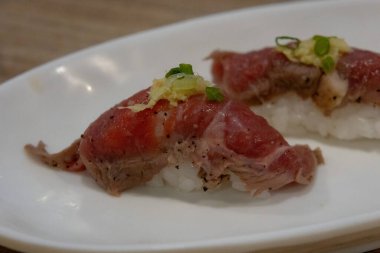İki parça Wagyu bifteği, zencefilli ve yeşil soğanlı nigiri sushi, beyaz bir tabakta..
