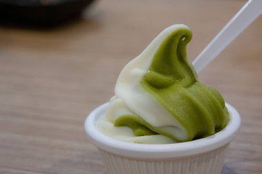 Küçük bir fincan kıvrımlı kibrit ve vanilyalı dondurma, beyaz plastik bir kaşık ve ahşap bir masa..