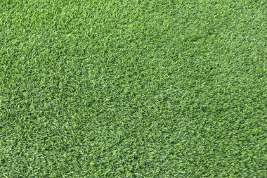 yemyeşil suni bir çimenliğe yakın çekim. Çimenlerin sentetik yaprakları mükemmel bir şekilde hizalanmış ve halı benzeri bir arka plan oluşturuyor.