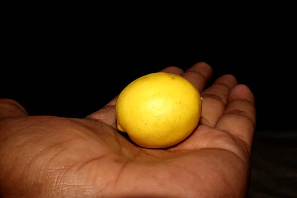 Elinde siyah arkaplanı olan taze sarı limon.