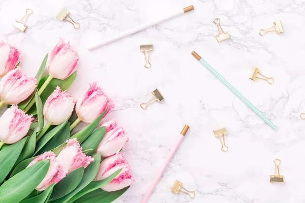 Pink tulips with festive stationary on white marble background. Feminine job, gender equality, home office and career concept. Copy space Top view. Horizontal