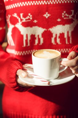 Şeker kamışı bir kapuçino bardağı tutan kız. Noel tatil kavramı. Tatil arka plan. Sıcak sesi. Dikey