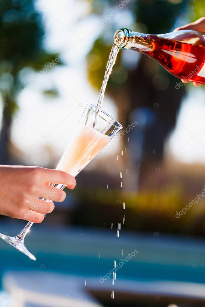 Waiter is pourring sparkling wine into a woman glass at the outdoor party.  Celebration concept. Event, party, wedding background. Toned image. Vertical