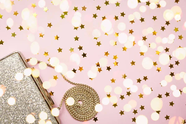 Festive evening golden clutch with star sprinkles on pink. Holiday and celebration background. Luxury accessories and party concept. Horizontal, bold light bokeh background