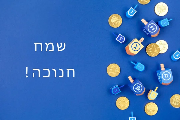 Fundo azul escuro com dreidels multicoloridos e moedas de chocolate e Happy Hanukkah redação em hebraico — Fotografia de Stock