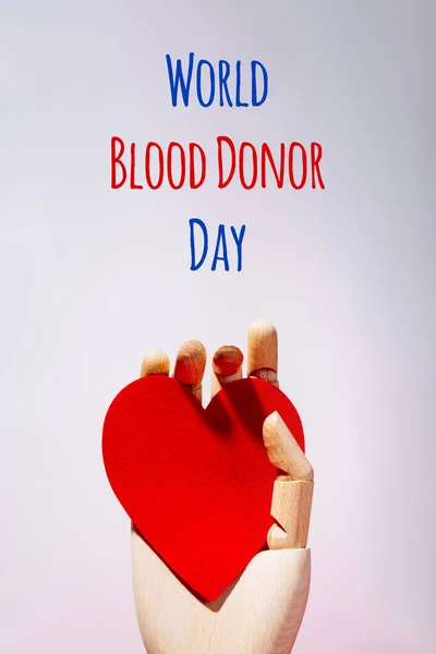 Wooden hand with big red heart in a giving gesture. World Blood Donor Day wording — Stock Photo, Image