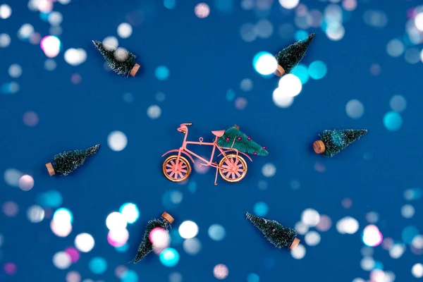 Fiets met kerstboom omgeven door besneeuwde bomen op klassiek blauw met feestelijke kleurrijke bokeh Stockfoto