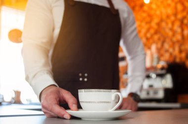 Bir fincan kahve barda tutan önlük yakışıklı barista resim kırpılmış Cafe counter. Odak Kupası