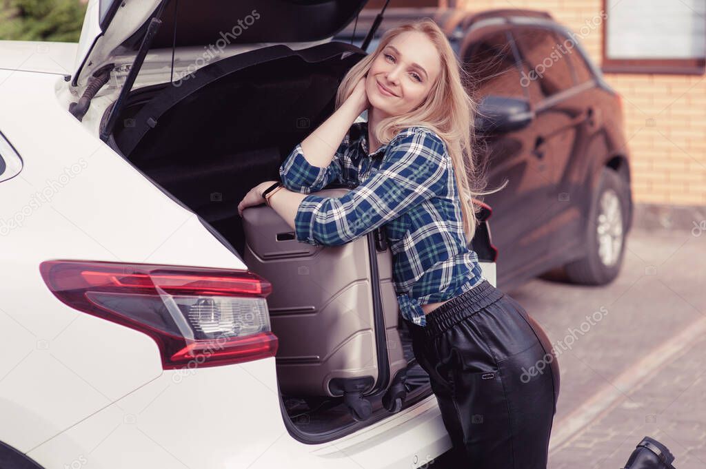 A young woman putting her luggage in the trunk of a car