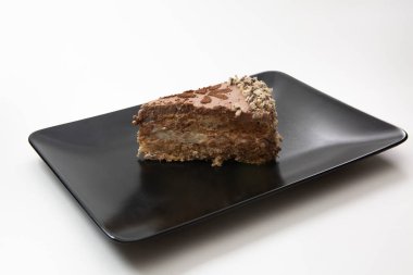 Siyah dikdörtgen bir tabakta ve beyaz arka planda bir parça kek.